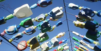 Photo of empty laundry soap containers threaded onto metal posts in the shape of a roof frame. Viewer is underneath the image.